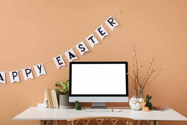 Workplace with computer, tree branches and Easter eggs in vase near color wall