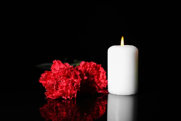 Burning candle with carnation flowers on dark background. Mourning concept