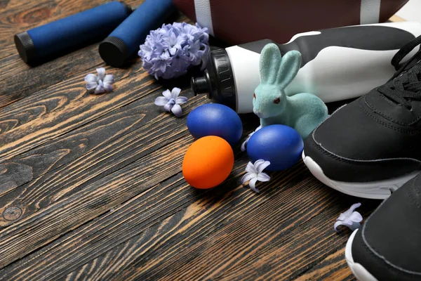Sports equipment with Easter eggs, rabbit and flowers on dark wooden background, closeup