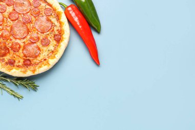 Delicious pepperoni pizza and jalapeno peppers on blue background