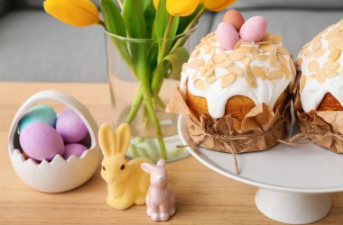 Stand with Easter cakes, painted eggs, bunnies and tulip flowers on table in living room