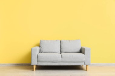Stylish grey sofa near yellow wall