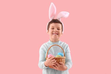 Cute little boy with bunny ears and Easter basket on pink background