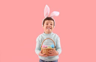Cute little boy with bunny ears and Easter basket on pink background