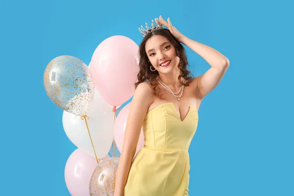 Beautiful young woman in prom dress and with balloons on blue background