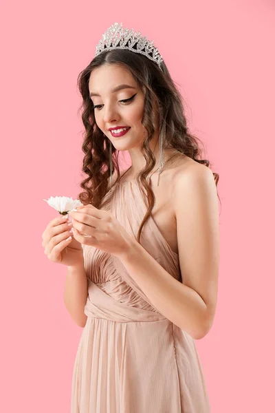 Beautiful young woman in prom dress and with flower on pink background