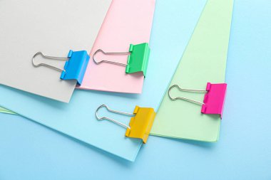 Paper sheets with binder clips on color background, closeup