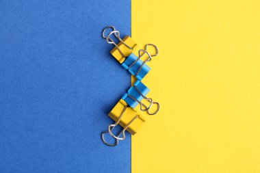 Blue and yellow binder clips on color background