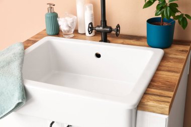 Table with sink, bath accessories and houseplant near beige wall, closeup