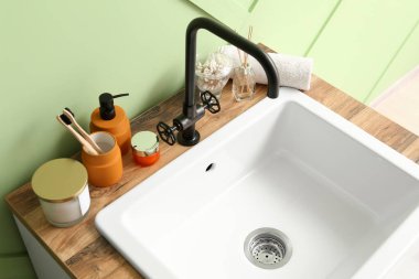 Table with ceramic sink and bath accessories near green wall