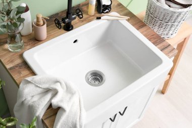 Table with ceramic sink, bath accessories and eucalyptus in vase near green wall