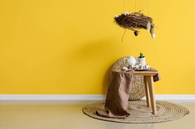 Tea set, cotton flowers and beautiful Easter decor on table near yellow wall