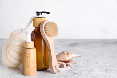 Bottles of cosmetic products, sponge and massage brush on light background