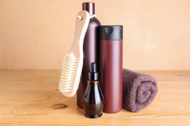 Bottles of cosmetic products, massage brush and towel on wooden table against color background