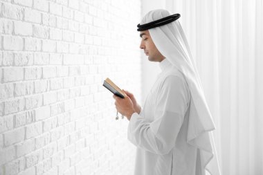 Praying Muslim man with Koran near white brick wall