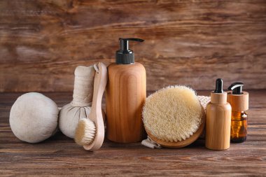 Massage brushes, herbal bags and cosmetic products on wooden background
