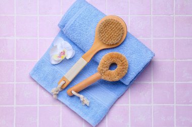 Massage brushes, towel and flower on color tile background