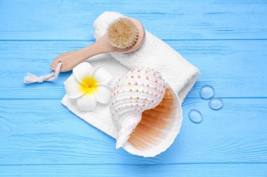 Massage brush, towel, seashell and flower on color wooden background