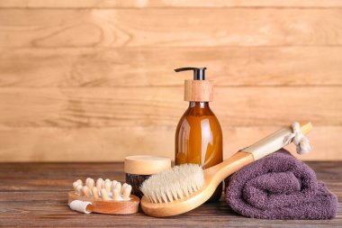 Massage brushes, cosmetic products and towel on wooden table