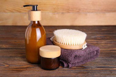 Cosmetic products, massage brush and towel on wooden table