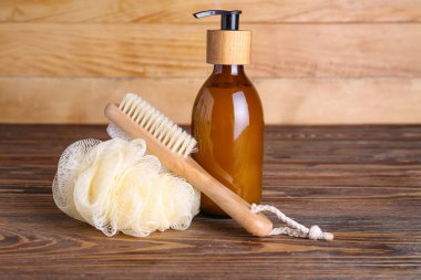 Massage brush, bath sponge and bottle of cosmetic product on wooden table