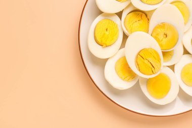 Plate with halves of delicious boiled eggs on beige background