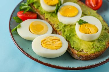 Plate with delicious avocado toast, boiled eggs and tomatoes on blue background