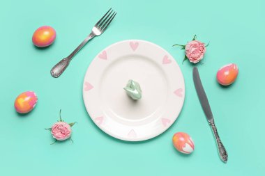 Table setting with Easter rabbit, eggs and flowers on mint background