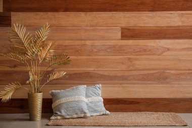 Stylish decorative pillows and golden palm leaves near wooden wall