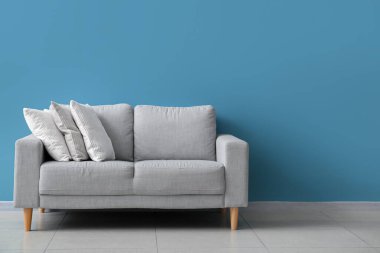 Stylish decorative pillows on cozy grey sofa near blue wall