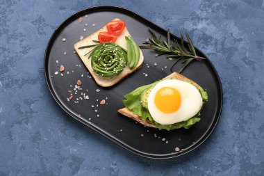 Plate with delicious avocado toasts and fried egg on blue grunge background