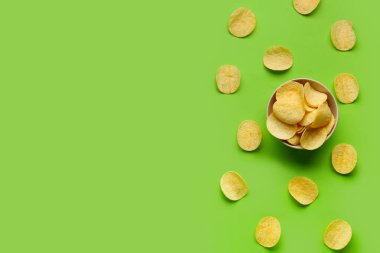 Bowl with delicious potato chips on green background