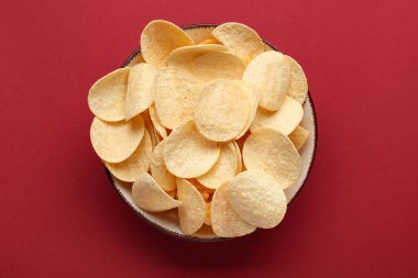 Bowl with delicious potato chips on red background