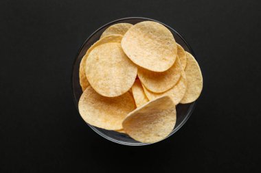 Bowl with delicious potato chips on black background