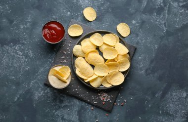 Plate with delicious potato chips, sauce, ketchup and sea salt on blue grunge background