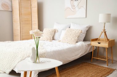Vase with ranunculus flowers and eyeglasses on table in interior of bedroom