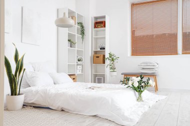 Interior of light bedroom with flowers in vase and houseplants