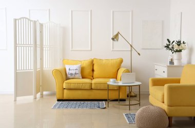 Interior of light living room with flowers in vase, sofa and armchair
