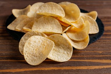 Heap of delicious potato chips on brown wooden table