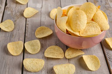 Bowl with delicious potato chips on grey wooden background