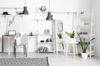 Interior of modern atelier with tailor's workplace, shelving units and mirror