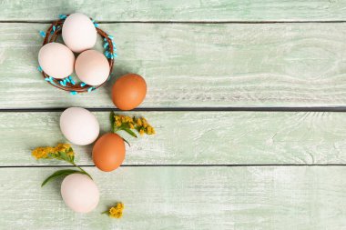 Easter eggs and goldenrod flowers on green wooden background
