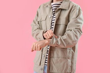 Young man rolling up his sleeve on pink background