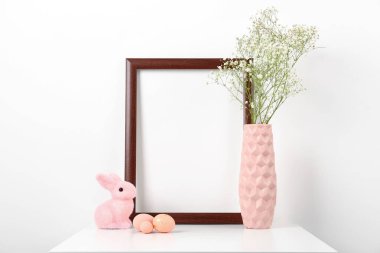 Blank frame, vase with gypsophila flowers, Easter eggs and bunny on white background