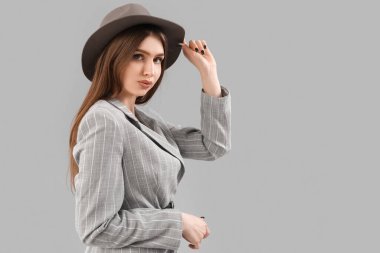 Stylish young woman in jacket and hat on grey background