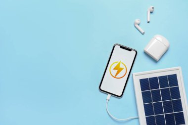 Portable solar panel with mobile phone and earphones on blue background