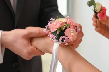 Young man tying corsage around his prom date's wrist, closeup