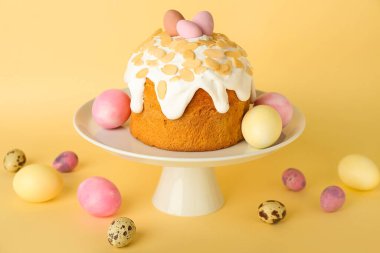 Stand with Easter cake and painted eggs on yellow background