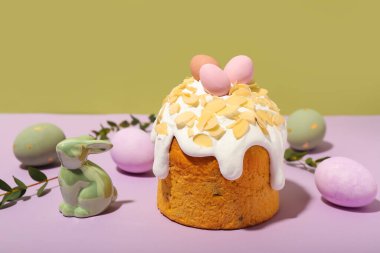 Easter cake, painted eggs and bunny on lilac table against green background