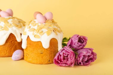 Easter cake, painted eggs and tulip flowers on yellow background